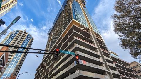 An image of a large glass and concrete new tower in Atlanta with yellow construction cranes affixed to it under blue skies. 