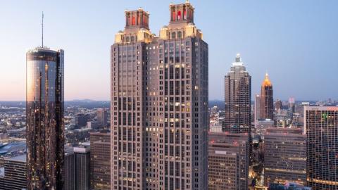 A photo of a large concrete skyscraper under blue purple skies in downtown Atlanta with many buildings and trees in the distance.