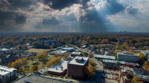 An aerial photo of a city with a much larger city in the distance over autumn trees.