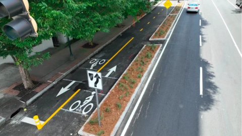 A photo of a bidirectional bike lane beside a wide street near many green trees in downtown Atlanta. 