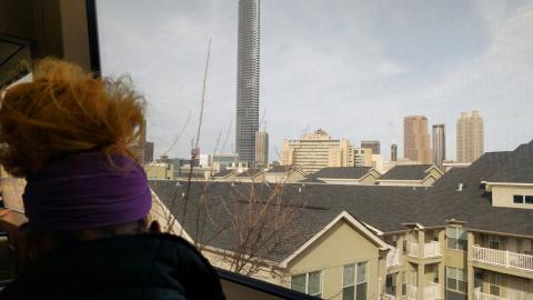 a photo of a woman on a marta train looking out the window to a giant new skyscraper under cloudy skies.