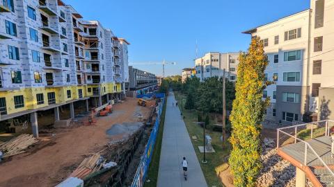 A photo of a person on a scooter near many large buildings on a long concrete pathway. 