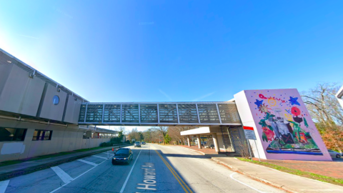 An image of a bridge under blue skies at a transit station leading between parking lots and trains.