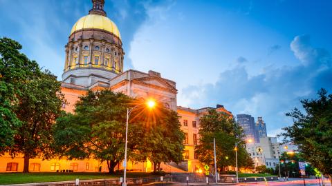 An image of Georgia's capitol shown under blue skies with a wide street in front near many trees.