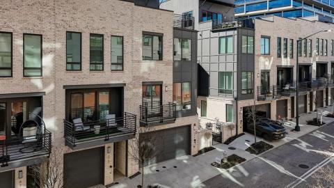 A row of modern-style townhomes with white interiors and rooftop decks and balconies in the shadow of tall new buildings in Atlanta. 