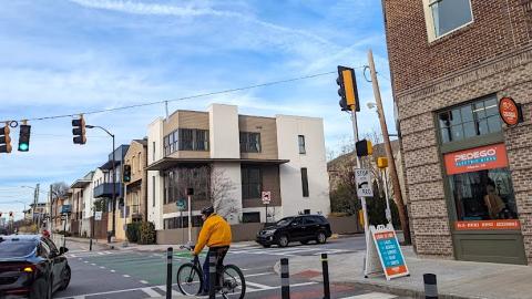 A photo showing conditions around a multipurpose trail through a city next to a wide street with many buildings and modern style houses around. 