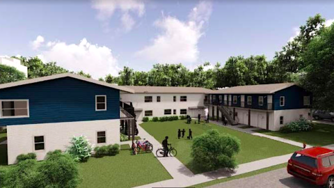 An image showing an apartment complex fixed up near a wide street across the street from a park.
