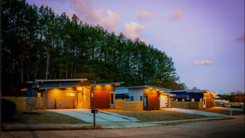 A row of modern homes with midcentury modern designs under purple blue skies in Atlanta with white open modern interiors and a wide street in front.