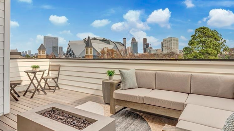 A photo of a row of townhomes built near downtown Atlanta with modern exteriors and rooftop decks shown under blue skies near older homes on the street. 