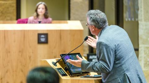 A photo of a man at a dais pleading to many people on a council. 