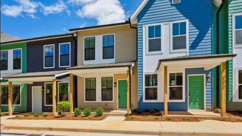 A new row of homes with bright facades next to a parking lot under blue skies in Atlanta. 