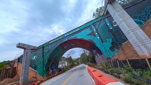 A photo of two large pillars of concrete next to an arched bridge over a roadway with plastic piles. 