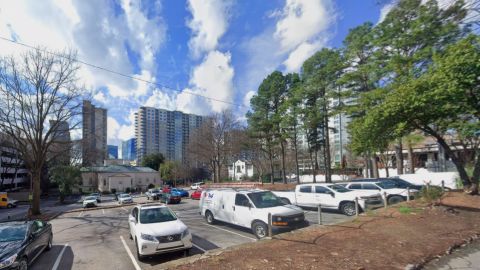 An image of a parking lot site near several busy streets and businesses and a long line of tall trees in Midtown Atlanta. 