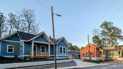 A photo showing six brightly colored cottages under a blue sky near a busy road in Atlanta with a courtyard and fire pit in between. 