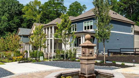 A photo of a new neighborhood with many new homes and a central green with nature trails and a small waterfall in the woods next door.