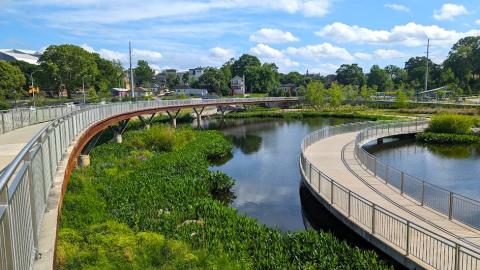 A beautiful new green park with two large bridges and a large pond under blue skies with clouds.