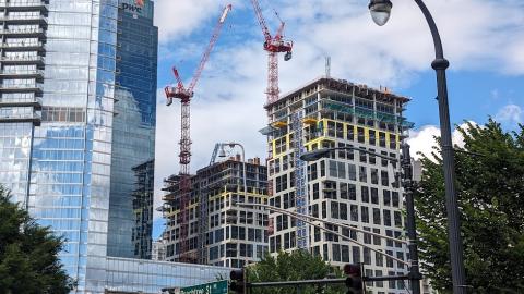 A photo of a large two-tower development make of concrete with tall red cranes over the top.