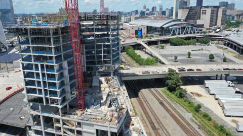 A drone photo showing a huge construction project underway next to railroad tracks in Atlanta beside a huge angular stadium and empty lot.