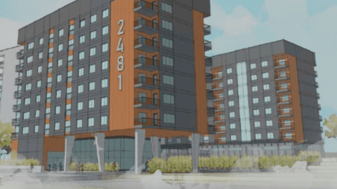 An image showing a site where a large apartment project is proposed under blue skies with a gray and orange facade and many balconies.