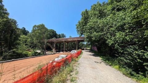 A photo of a wide gravel trail and an orange fence beside a lot of construction and trees in Atlanta.