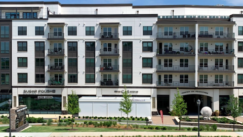 An image of a white, black, and grey building under blue skies next to a wide road with shops at the bottom and fancy interiors near Atlanta. 