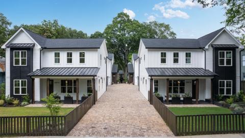 A photo of a large row of duplexes under blue skies with green yards and a wide drive between, with white modern-rustic interiors in Atlanta.