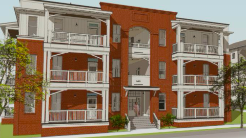 A rendering of a new small brick building under blue skies on a corner lot next to another housing building on a wide street.