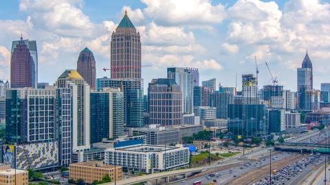 A image of skyline in Atlanta with a huge highway beside under blue skies and many clouds.