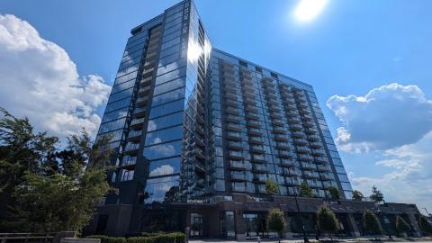 A photo of a large glassy building with many balconies over a wide road against a blue sky.