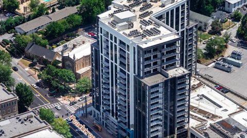 An aerial image of a large new black and white building standing over wide road and a shopping center near many trees in Atlanta.