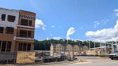 an image of a mixed-use project site that's being built beside a wide road under blue skies with townhomes in the back. 