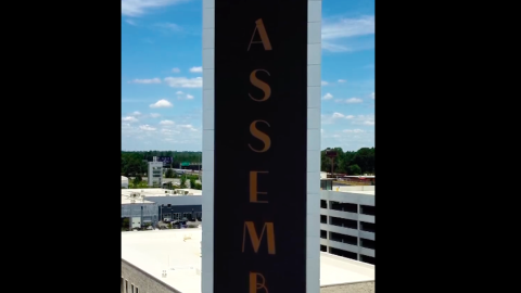 A photo of a large LED billboard tower with a metal backing standing over a park in Atlanta with blue skies overhead.