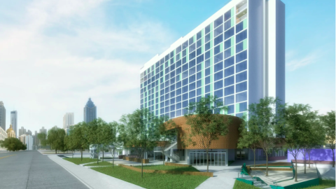 An image of a large white empty hotel near huge parking lots and a wide road under blue skies.