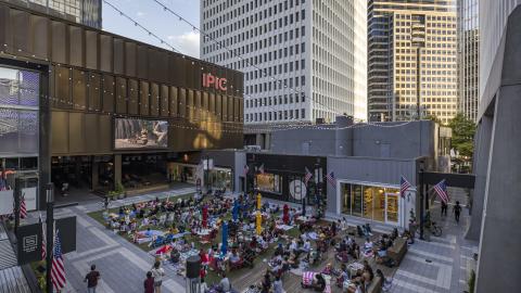 A photo of a large mixed-use community shown under blue skies with many buildings standing and people socializing in open spaces.