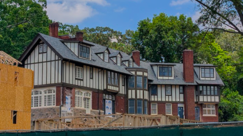 A large construction site with a historic tudor mansion on a hill and many homes being built under blue skies next to many trees in Atlanta.