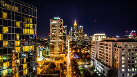 A long city skyline at night as seen from above with many lighted buildings and a glowing street.