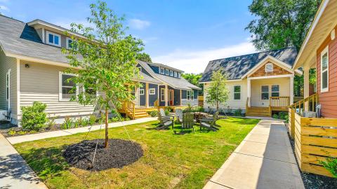 A photo of a small village of town houses with a green and fire pit in the middle with white modern interiors.