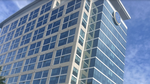 A glassy new building with a large rooftop area shown next to a wide street under blue skies in Atlanta.