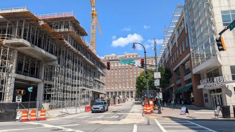 a large construction site with a concrete tower, a wide street, and with The Biltmore House in the background.