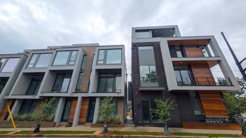 A photo of a large modern townhome complex with wood and gray-black exteriors on a corner in Atlanta, with modern white interiors on the inside. 