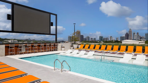 A photo showing a large new modern-style student housing building in Atlanta under blue skies with a large pool on the roof and white modern interiors. 