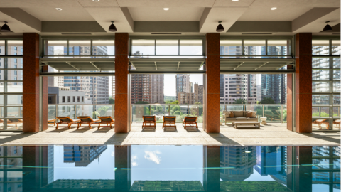 an indoor pool at a nice modern condo building overlooking a large city under blue skies.