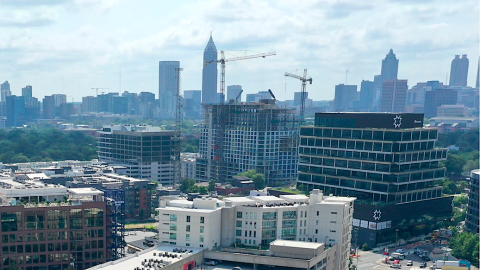 A drone photo high over new buildings in a large new district of Atlanta under blue skies, with the main city in the hazy distance.