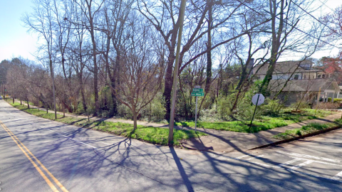 A corner of a development site under blue skies near wide streets in Atlanta with a sidewalk in front.