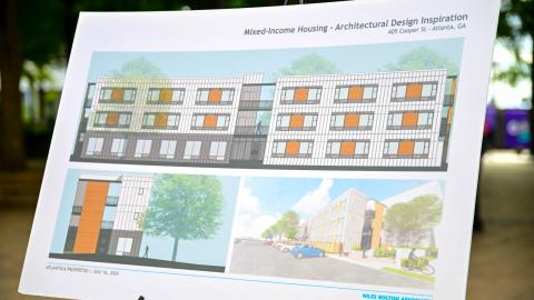 A board shown at a press conference with many new housing units arranged around a parking lot with many trees on the sides.