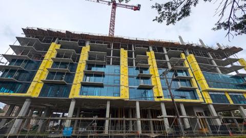 A construction photo of a glass and concrete building with a red crane over it, overlooking a wide street in Buckhead Atlanta. 