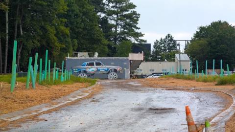 A corner site cleared of trees with a new road in the middle and a mural with a large car with big wheels on a wall beyond. 