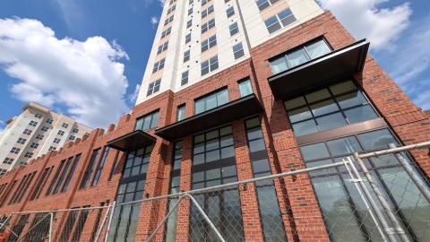 A photo of a brick and stucco and glass large new tower under blue skies next to a wide street in Atlanta.