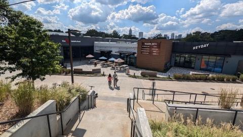 A photo of a large shoe store, Athlete's Foot, in a new Atlanta location in a gray and black building under blue skies near walkways. 