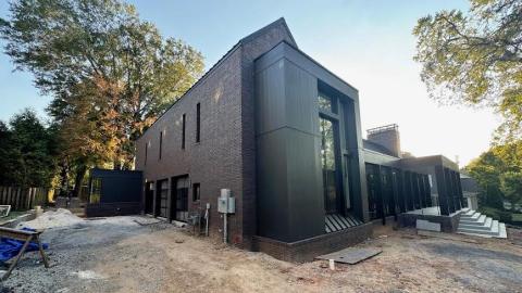 A photo of a brick and black modern house with glass and a large front yard in a leafy Atlanta neighborhood.